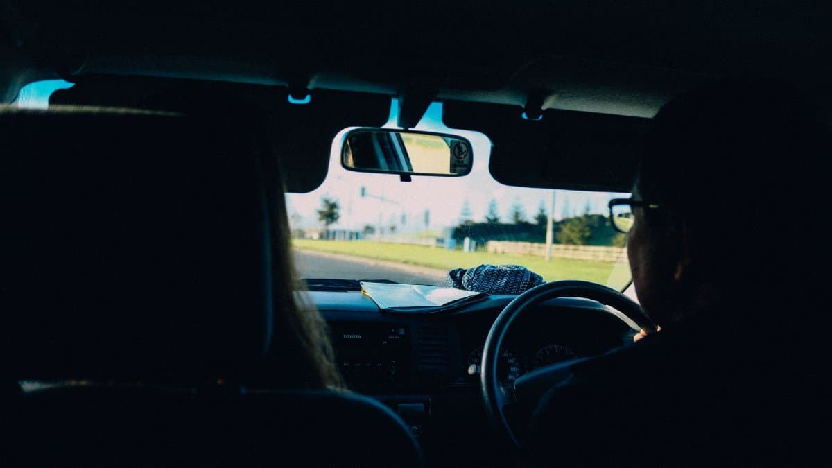 Back view anonymous person driving right hand drive car near female on passenger seat