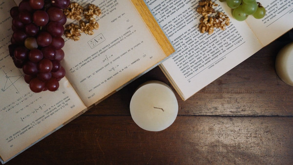 Aesthetic still life with grapes, walnuts, and open books by candlelight on a wooden table.
