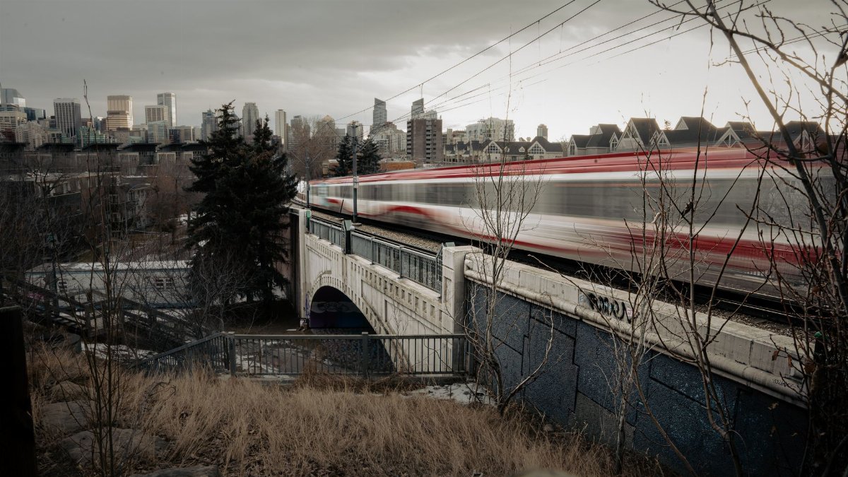 A high-speed train speeding across a bridge in Calgary with city skyline in the background.