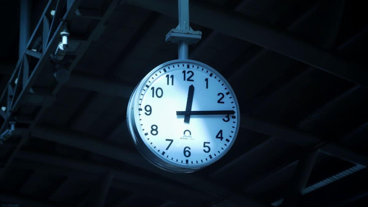 A large clock hanging at Dhaka railway station showing the time in a dimly lit environment.