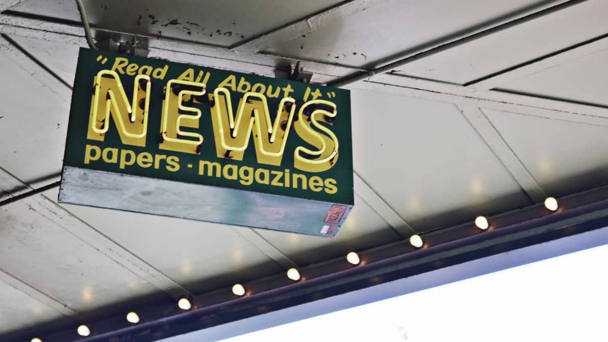 From below of illuminated signboard with news papers magazines inscriptions hanging on metal ceiling on street