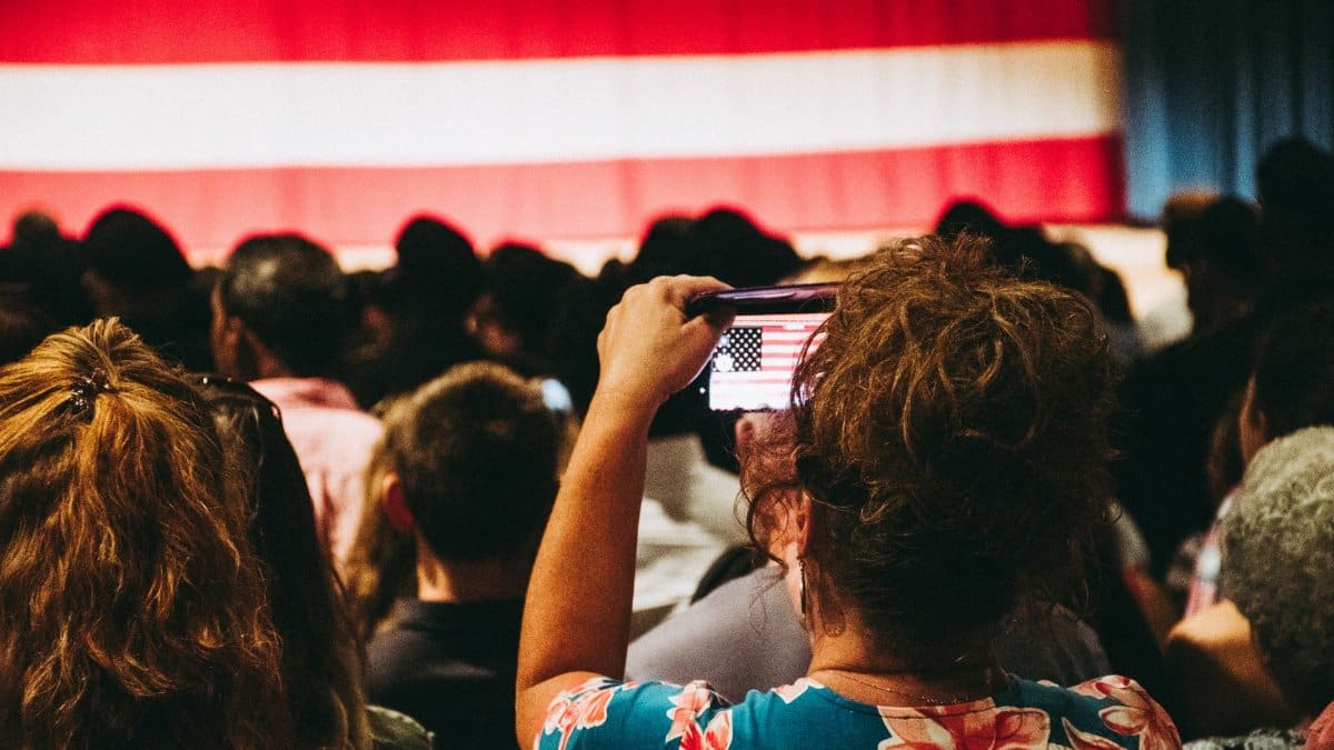 A crowd takes photos of an American flag at a busy indoor rally, encapsulating unity and patriotism.