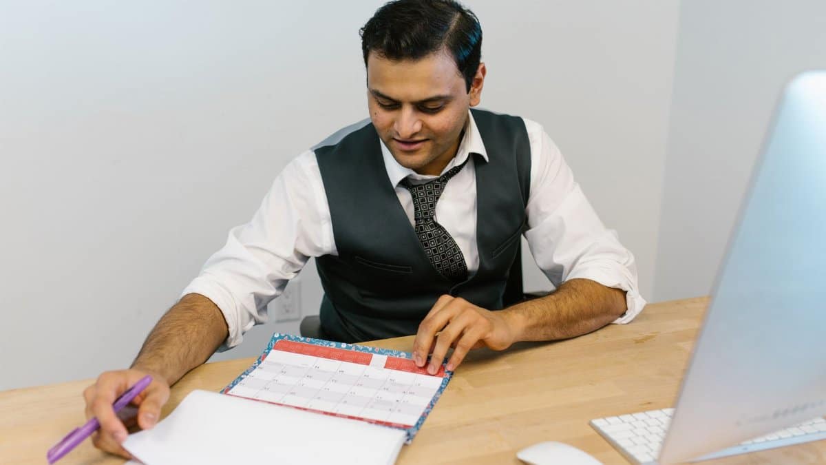 A businessman checks his schedule at a desk, referencing a calendar and making notes.