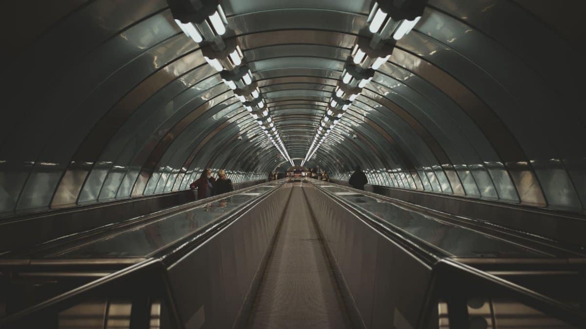 Futuristic underground tunnel featuring a moving walkway and illuminated ceiling.