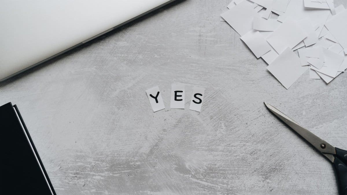 Artistic layout of paper cutouts forming 'YES' with scissors on a desk surface.