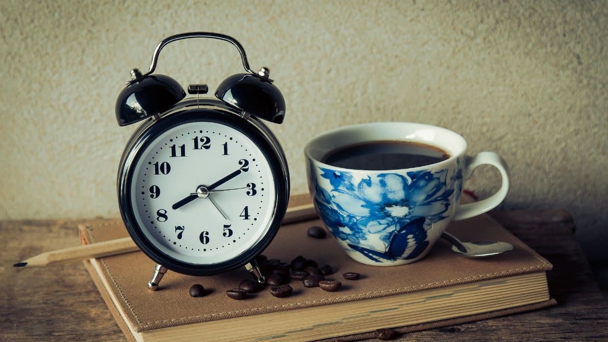 Cozy morning setup with a vintage alarm clock and floral coffee cup on a book. Perfect for capturing morning routines.