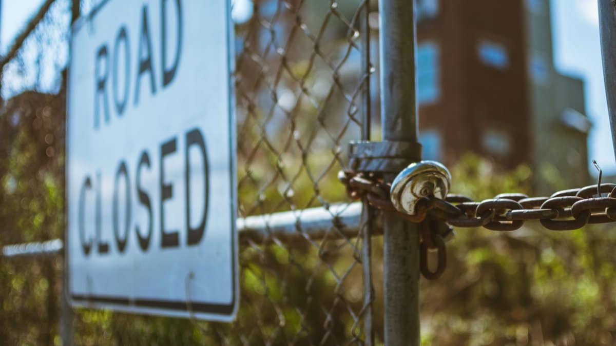 Close-up of a locked chain fence with a road closed sign, symbolizing security.