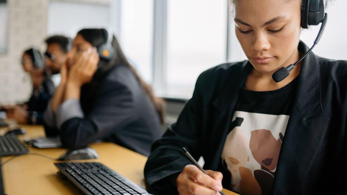 Focused call center employee using headset and writing notes at her desk, working efficiently.