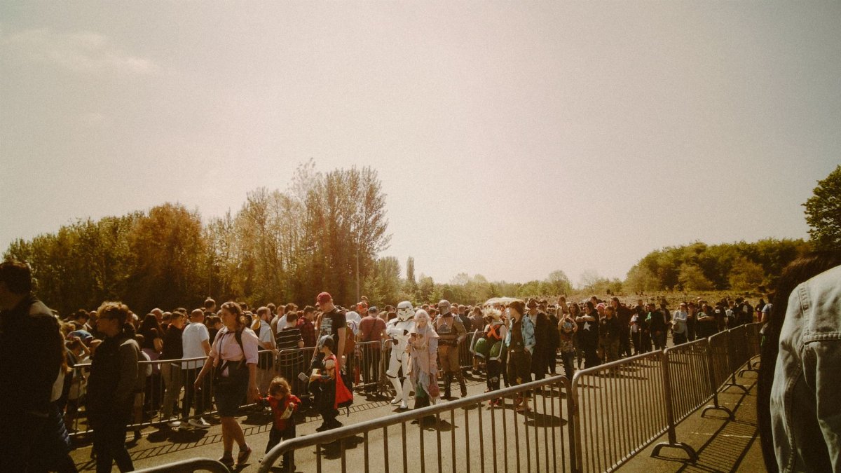 A large crowd in costumes waits in line at an outdoor festival on a sunny day.