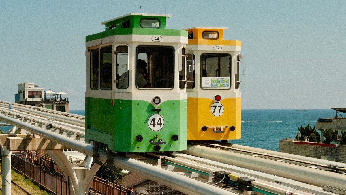 Vibrant monorail crossing over serene waters in Busan, South Korea.