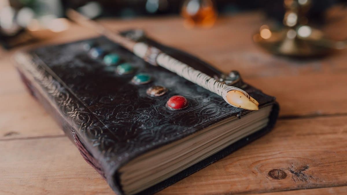 Close-up of a mystical spell book adorned with magical stones and a wand on wooden surface.