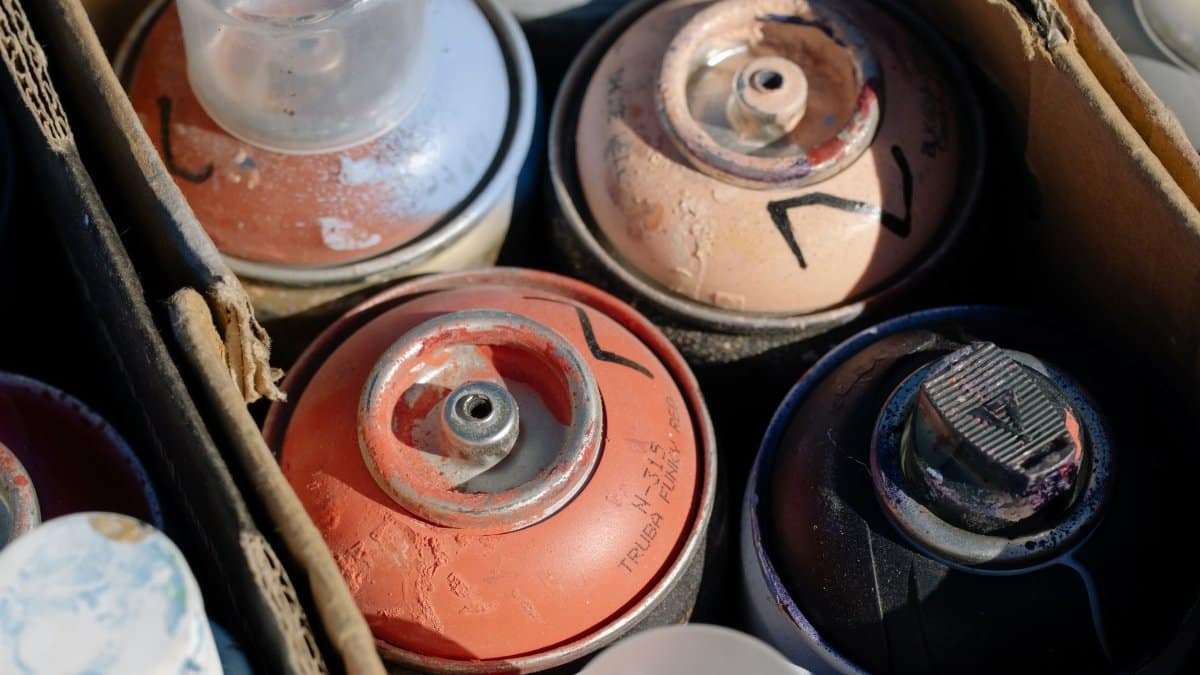 Detailed view of various spray paint cans in a cardboard box, showcasing art materials.