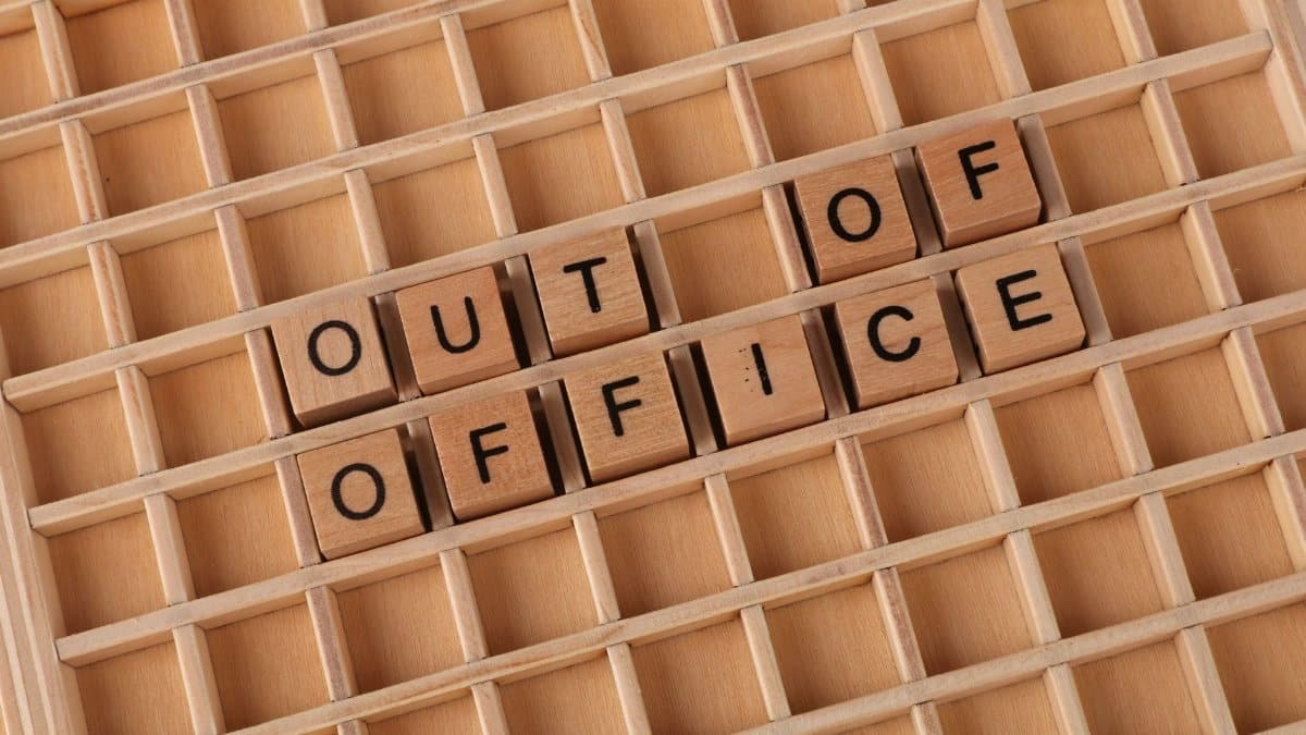 Close-up of wooden letter tiles spelling 'Out of Office' on grid layout background.