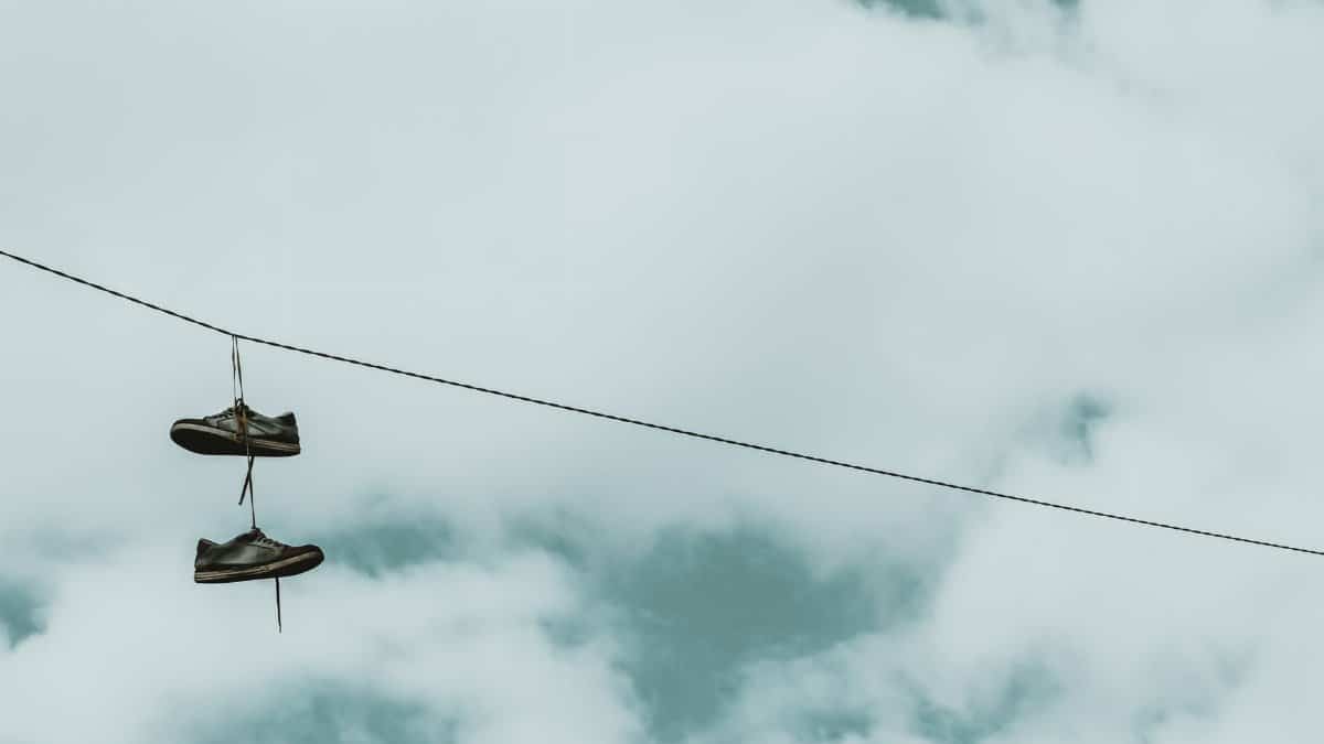 Pair of sneakers hanging on a cable wire amidst a cloudy backdrop, creating an intriguing still life scene.