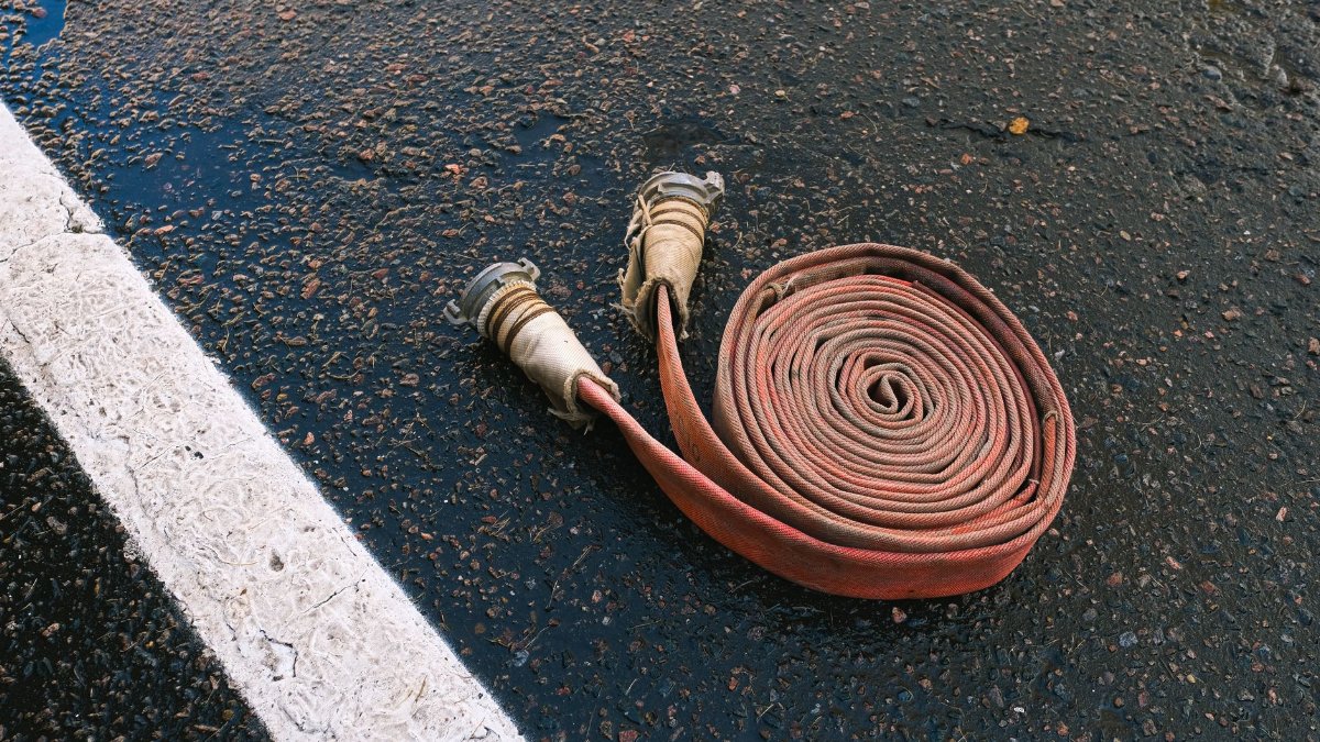 Close-up of a rolled fire hose lying on a textured asphalt road with a white dividing line.