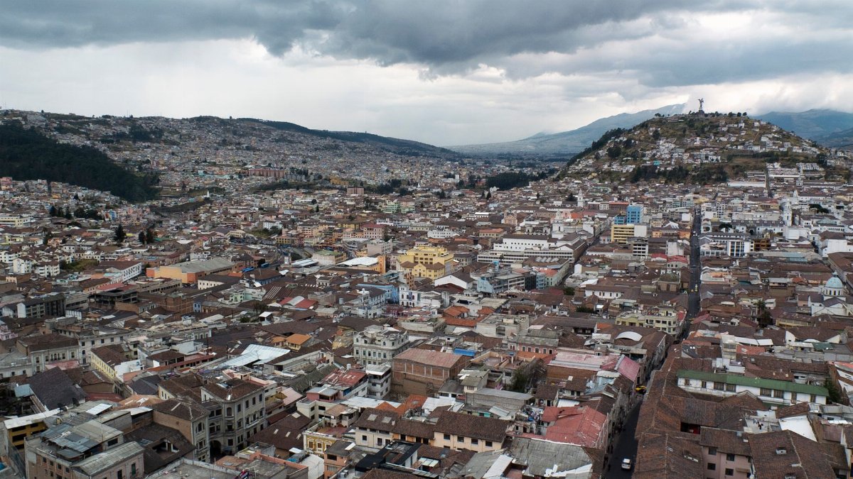 Expansive aerial view of Quito's historic cityscape with cloudy skies, featuring scenic hills and urban density.