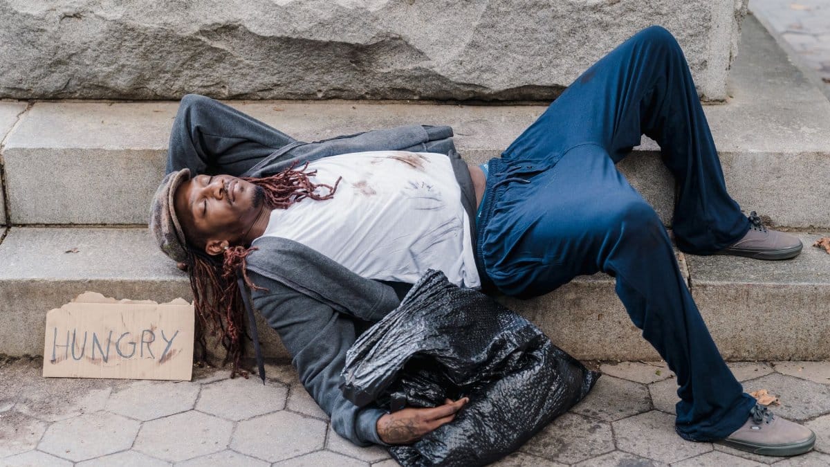 A homeless man resting on city steps with a cardboard sign reading 'Hungry'.