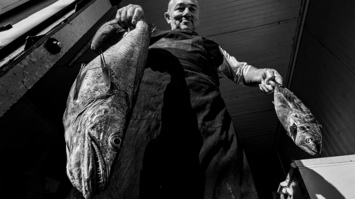 Black and white photo of a fisherman holding two fish at a seafood market in Istanbul.