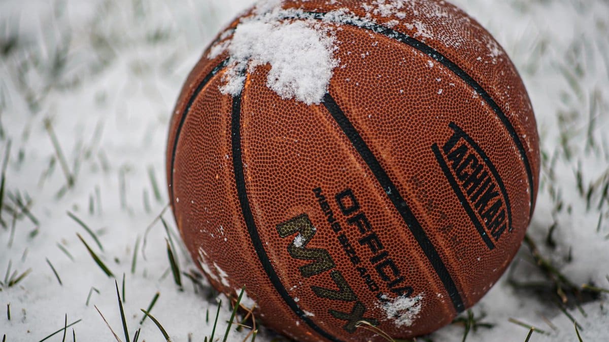 A close-up of a basketball resting on snow-covered grass, emblematic of winter outdoor sports.