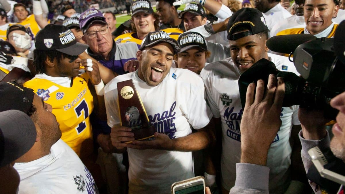 Football team celebrating their national championship victory with trophy and media.