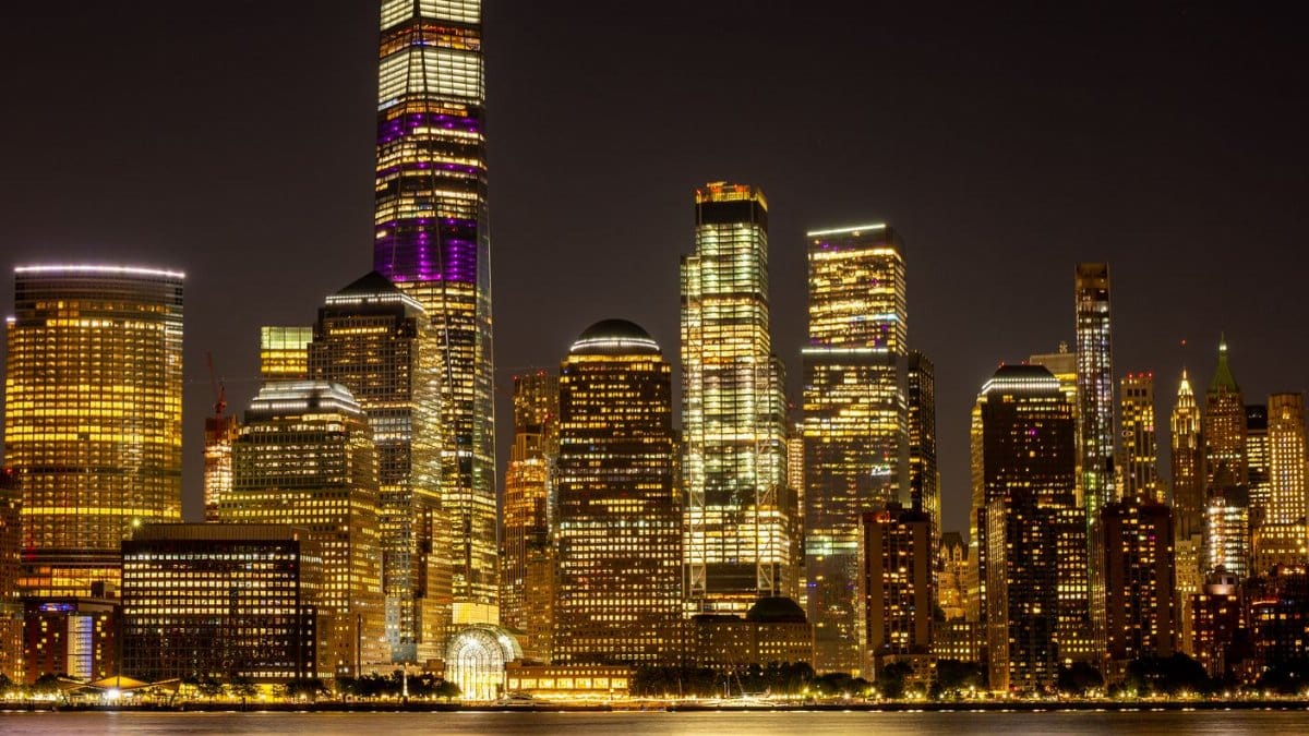 Stunning view of New York City's illuminated skyline and One World Trade Center reflecting on calm water at night.