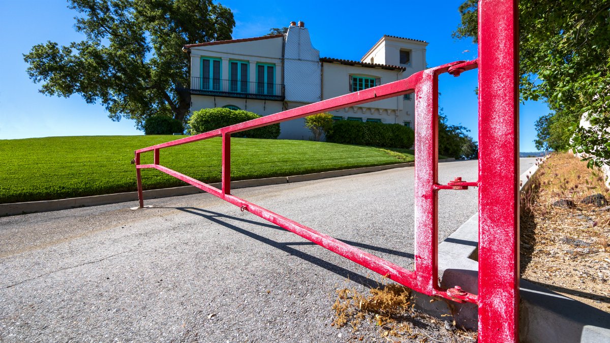 A bold red gate on a sunny day, marking the entrance to a beautiful hillside residence.