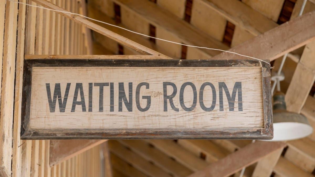 Close-up of a vintage wooden 'Waiting Room' sign in rustic surroundings.