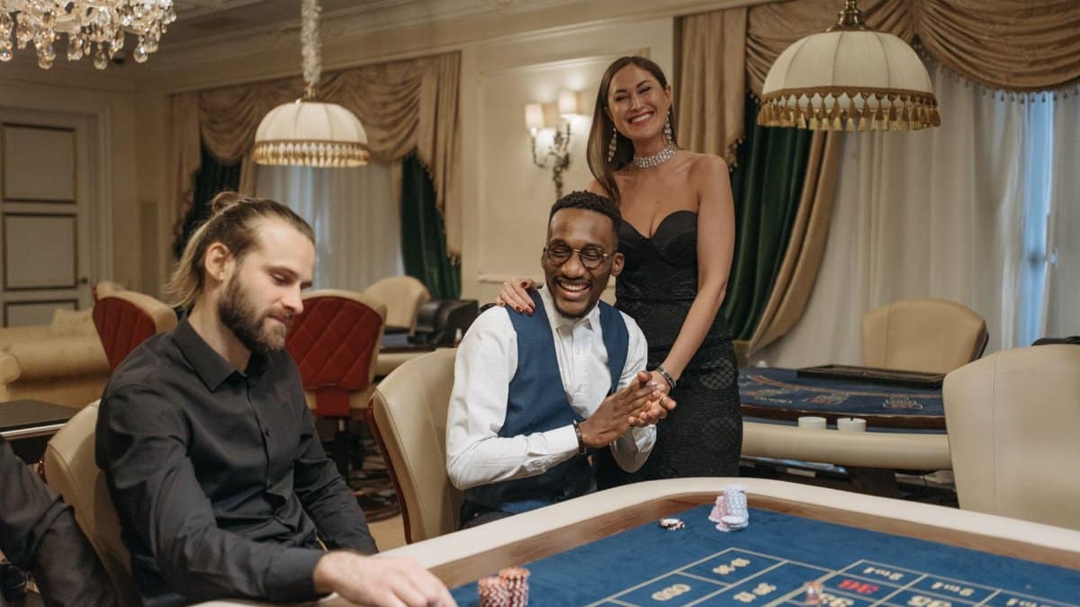 Three people enjoying a night at an elegant casino gambling table.