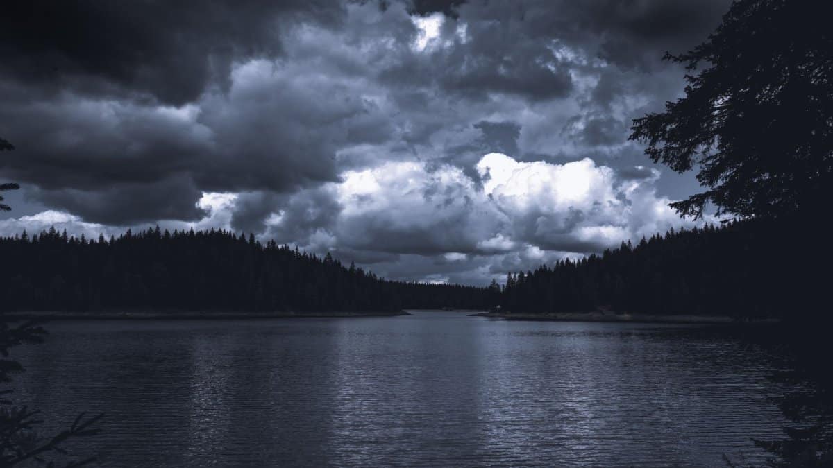 Moody landscape of a dark lake with stormy clouds over forested mountains in Žabljak.