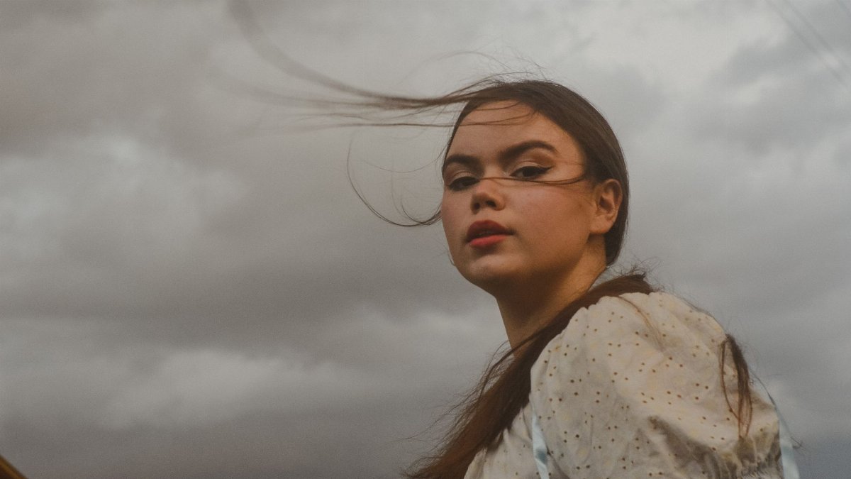 Artistic portrait of a young woman with wind-swept hair under an overcast sky, expressing beauty and emotion.