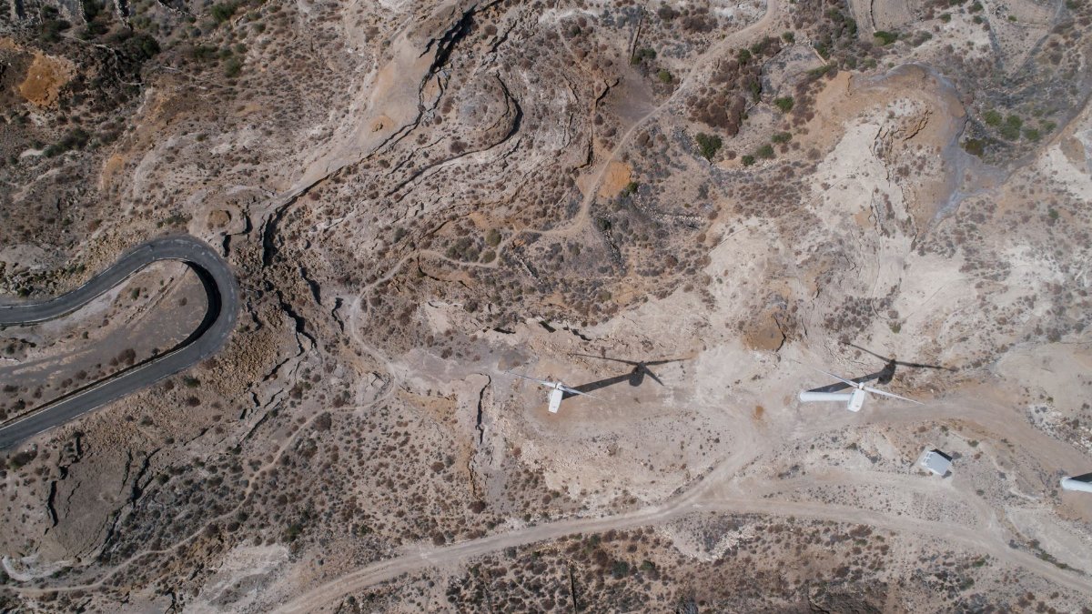 Drone shot of wind turbines in a dry, arid terrain with winding roads.