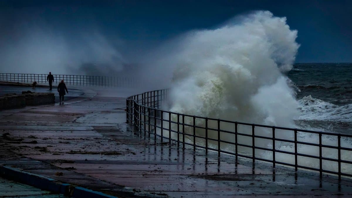 Powerful ocean waves crash against the seaside walkway, showcasing nature's forceful beauty.