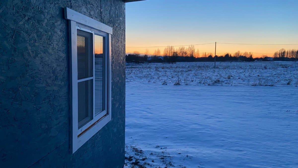 A serene winter landscape featuring a snow-covered field and house at sunset in Russia.