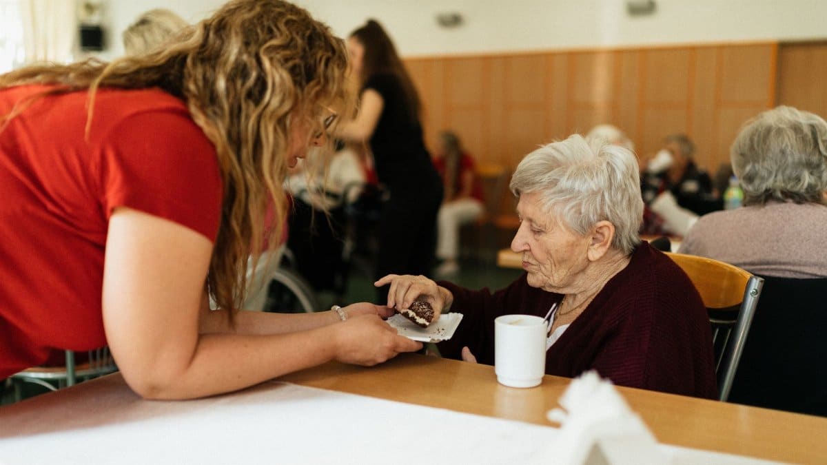 An elderly woman being assisted by a caregiver in a nursing home setting.