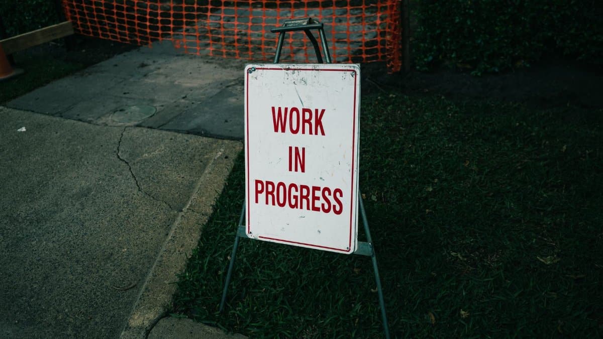 A 'Work in Progress' sign stands on a sidewalk next to safety barriers.