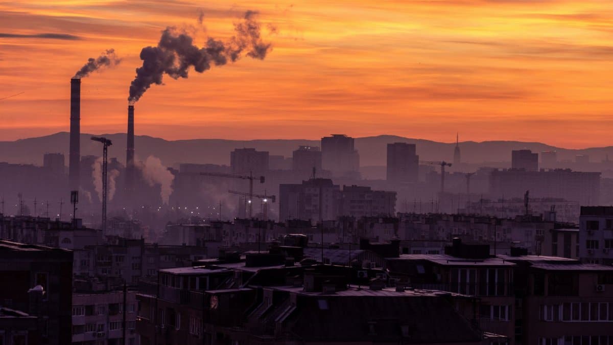 A city skyline with smokestacks emitting pollution, set against a vibrant sunset sky.