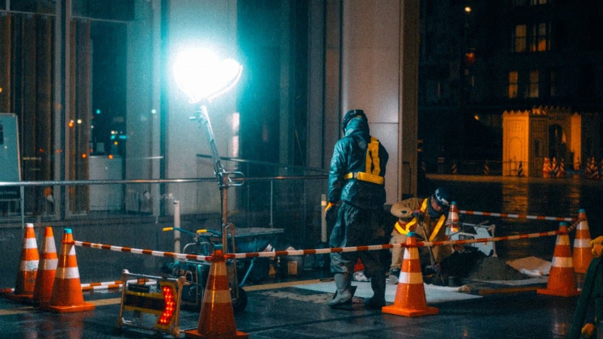 Construction workers at night in a city with bright lights and reflections.