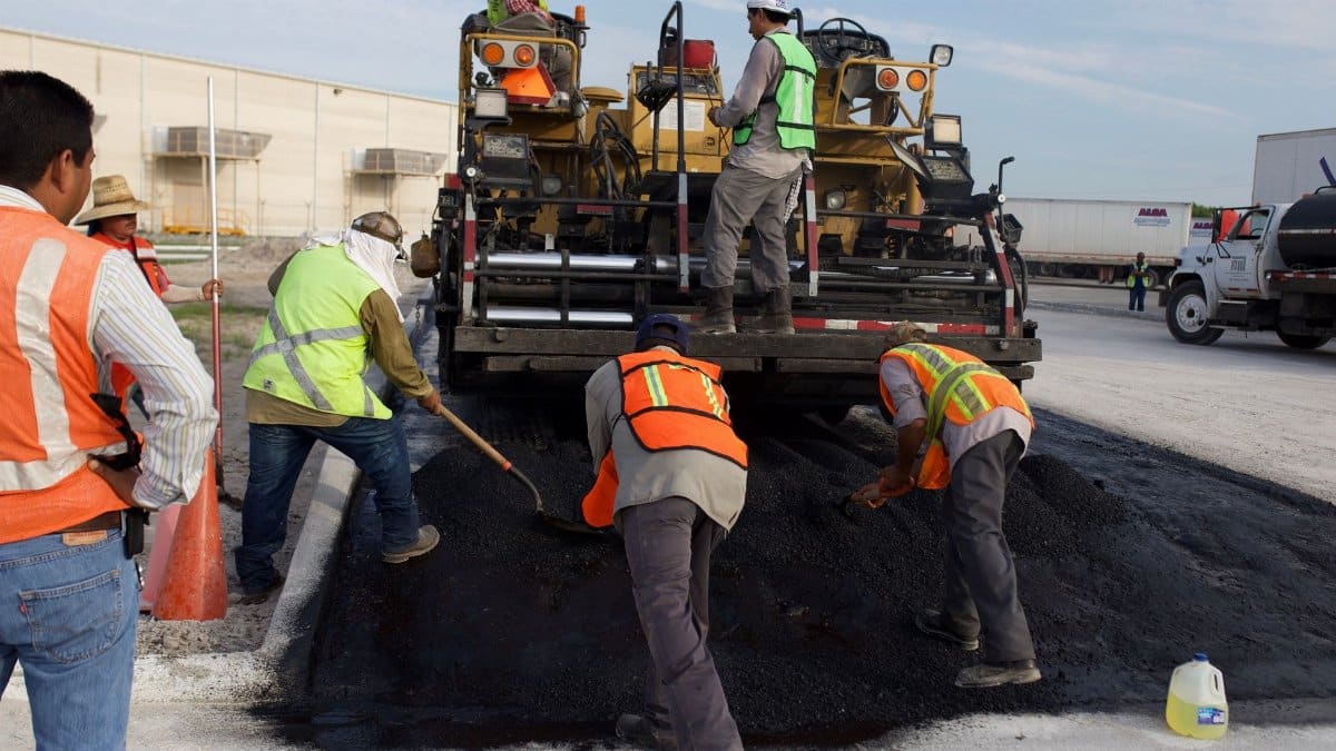 Construction workers laying asphalt on a road with heavy machinery.