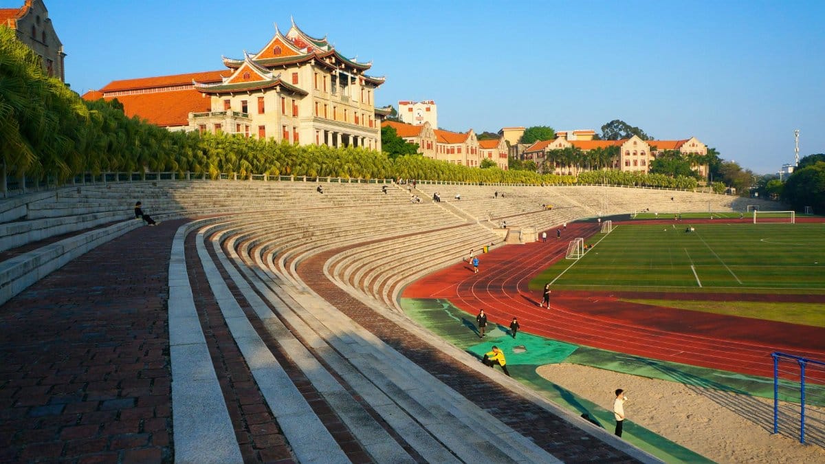 A school campus with traditional architecture overlooking a large track and field area during the day.