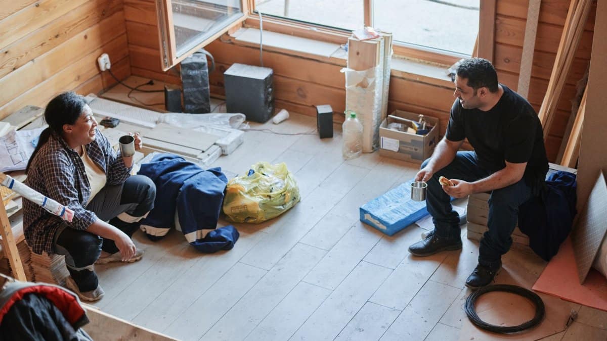 Two construction workers taking a break and chatting inside a wooden room during a renovation project.