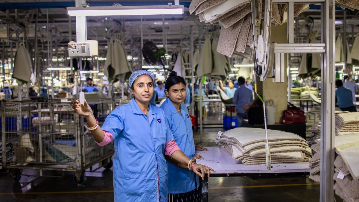 Two female textile workers operate machinery in an Indian factory, wearing blue uniforms.