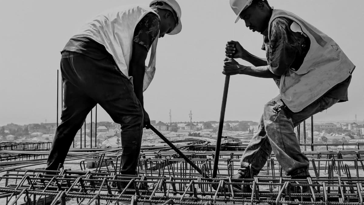 Black and white image of two construction workers reinforcing steel bars on a building site.