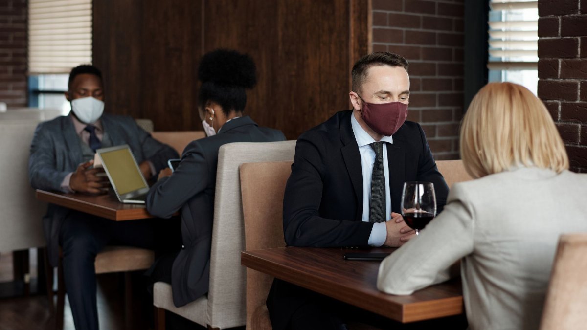 Office workers wearing masks in a café meeting, ensuring pandemic safety with social distancing.