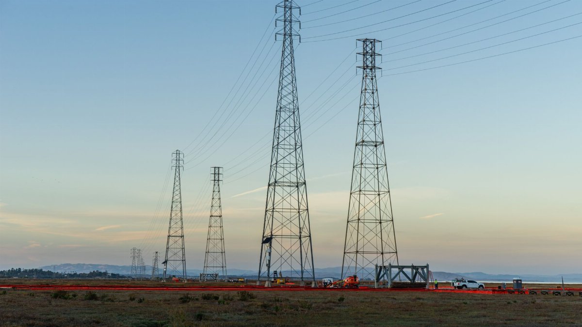 High voltage transmission towers with clear blue sky at dusk in an open field.