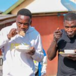 Two men relishing street food outdoors on a sunny day, capturing urban lifestyle.
