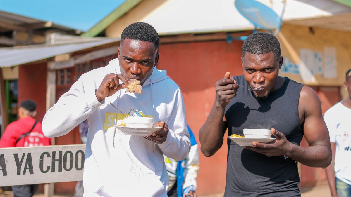 Two men relishing street food outdoors on a sunny day, capturing urban lifestyle.