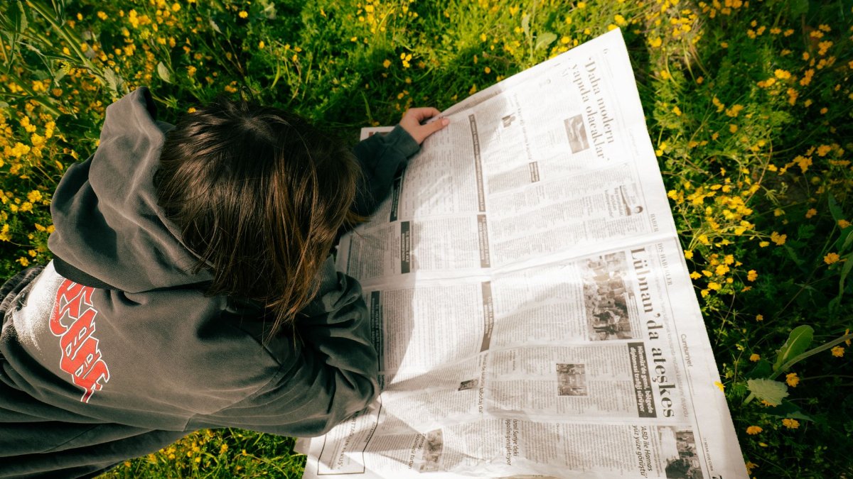 A young person enjoying reading a newspaper while lying on a flowery spring field.