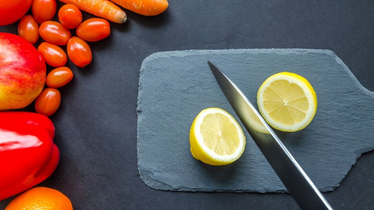 Top view of fresh produce including lemon, carrots, tomato, and peppers on a slate board.