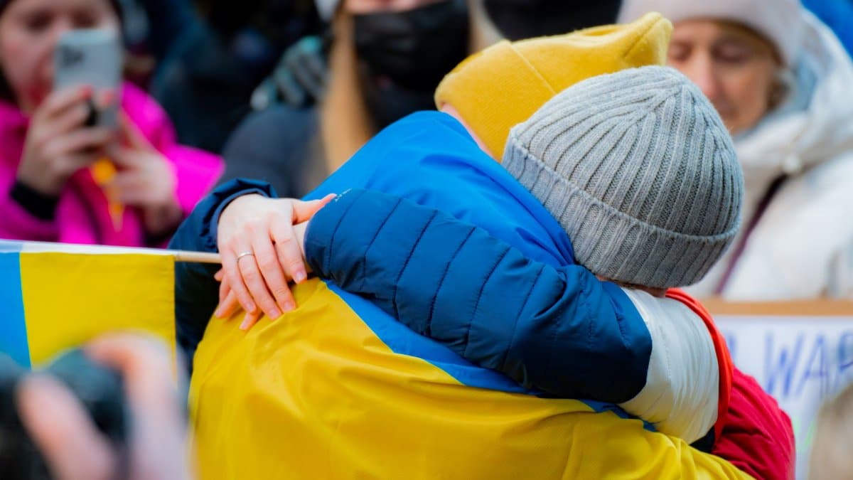 Close-up of two adults embracing at a New York protest, with people in background.